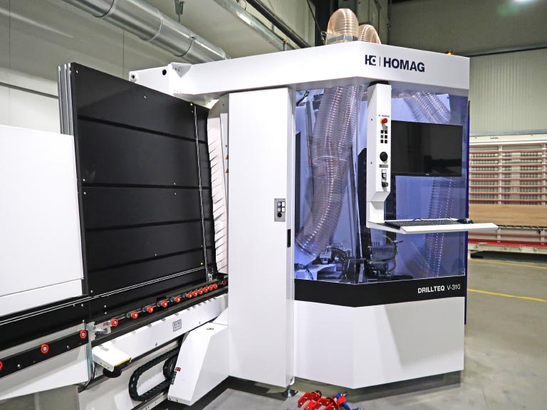 Weiße vertikale CNC-Bohrmaschine vom Typ Homag DRILLTEQ V-310 mit geschlossenem Arbeitsbereich, Display, Tastatur und Sichtfenster in einer Produktionshalle.