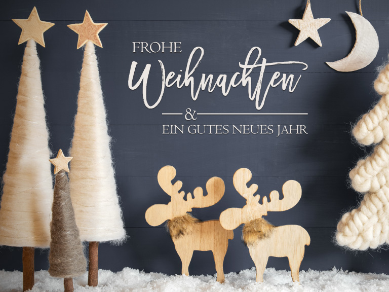 Weihnachtliche Dekoration mit Filzbäumen, zwei Holz-Rentieren mit Fellkragen, gestricktem Weihnachtsbaum sowie Schriftzug „Frohe Weihnachten & ein gutes neues Jahr“ auf dunkelblauem Hintergrund mit Schnee.