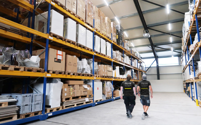 Menschen gehen durch das Lager der step one GmbH, um Materialien für Messebau und Logistik zu koordinieren.