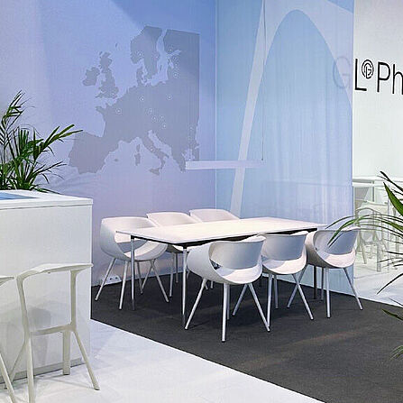 GL Pharma Messestand mit weißen Stühlen und Tischen, einem Tresen, dekorativen Pflanzen und einer stilisierten Europakarte an der Wand.