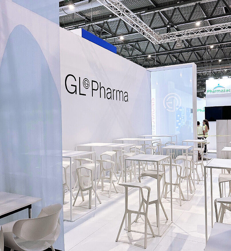 GL Pharma Messestand mit weißen Stehtischen und Hockern. Helle, offene Gestaltung mit modernem Design.