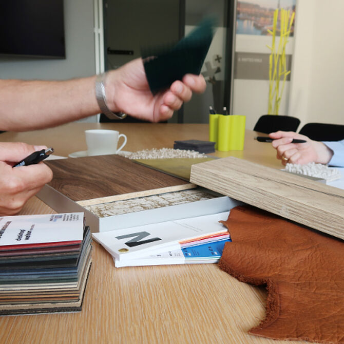 Nahaufnahme eines Beratungsgesprächs bei step one mit Materialmustern, darunter Holzoberflächen, Stoffe und Farbkarten, auf einem Tisch. Zwei Personen sprechen und vergleichen Muster.